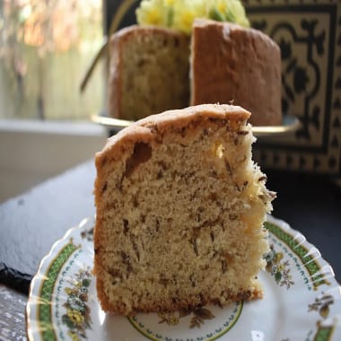 Old Fashioned Caraway Seed Cake slice on a plate with whole cake in the background.